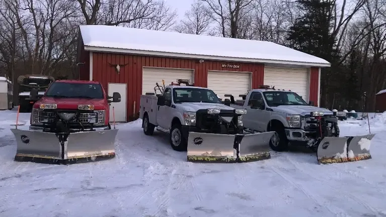 Pickup trucks fitted with snow plow blades parked at a shop in winter — landscaping insurance in Indiana.