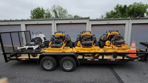 Commercial zero-turn mowers and equipment loaded on a tandem-axle landscaping trailer.