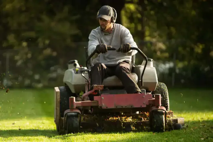 A landscaper mowing a lawn on a zero-turn riding mower as grass clippings fly — landscaping insurance in Oklahoma.